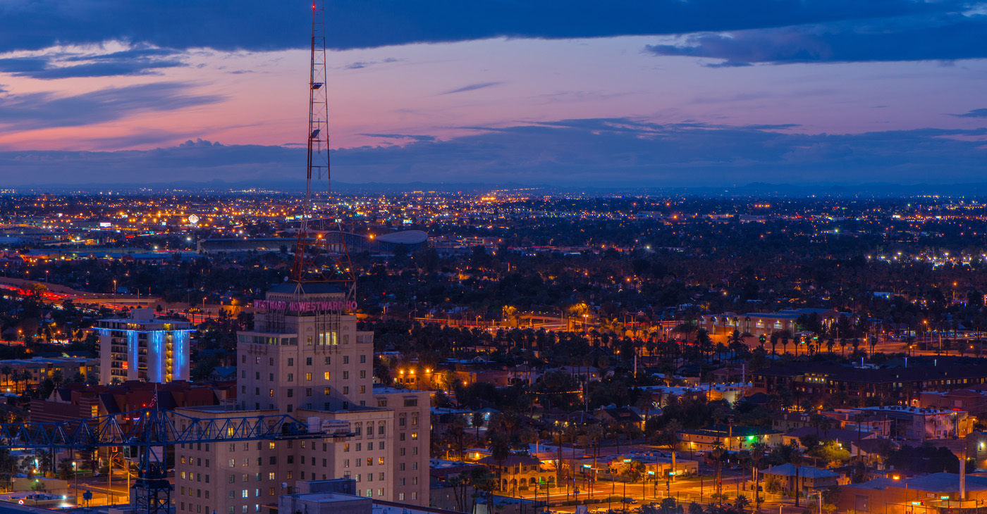 dusk aerial view over phoenix arizona commercial real estate downtown with street and building lights stretching off to the horizon under a purple, blue and orange cloudy sky