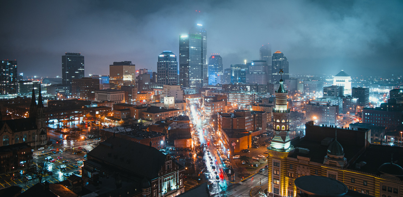 nighttime bird's eye view across downtown commercial real estate indianapolis indiana with the buildings and streets lit up and low clouds slightly obscuring the tops of skyscrapers