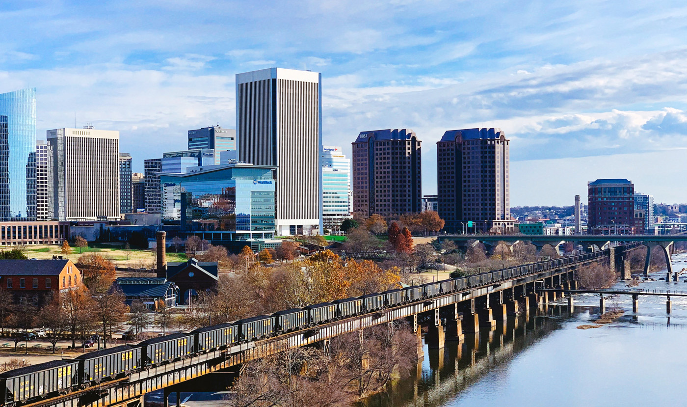 daytime aerial view from the james river waterfront of downtown richmond commercial real estate virginia office buildings with a long freight train on elevated waterside train tracks in the foreground