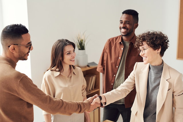 colleagues shaking hands displaying peer-to-peer recognition one of the top in-person employee recognition ideas in the new world of work image at offices.net