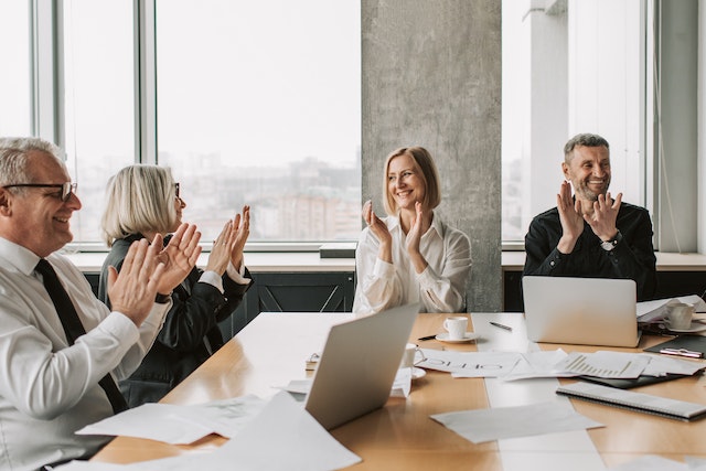 colleagues in business attire around boardroom table applauding and smiling image at offices.net