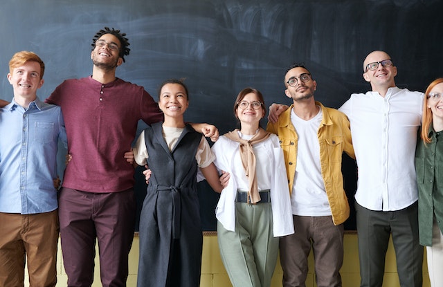 young colleagues standing together in a line with arms around each other smiling image at offices.net