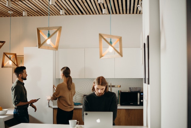 three colleagues gathered in kitchenette with two talking and another working on a laptop image at offices.net