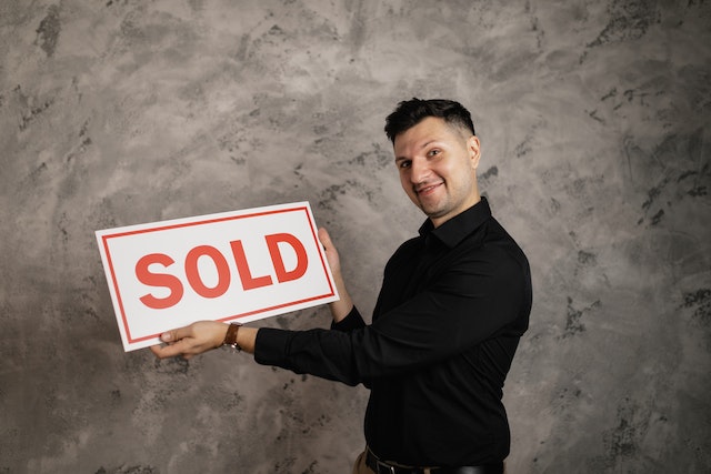 a man smiling and holding a sign that says sold image at offices.net