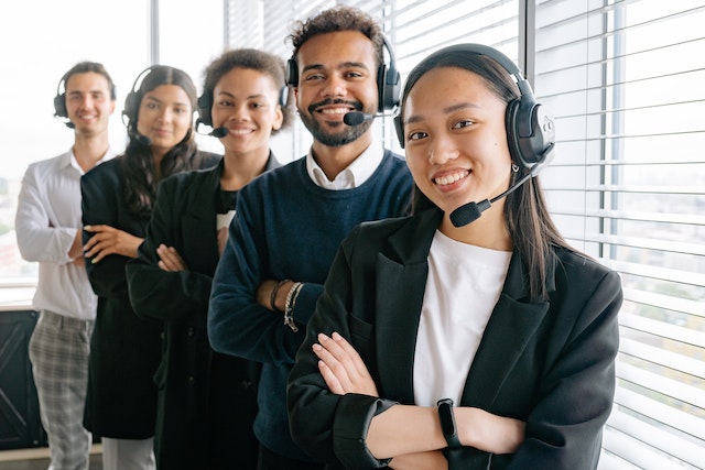 five smiling dark haired call centre workers in a line wearing microphoned headsets with crossed arms image at offices.net