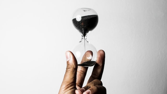 hand holding an hourglass with black sand spilling down into the bottom chamber image at offices.net