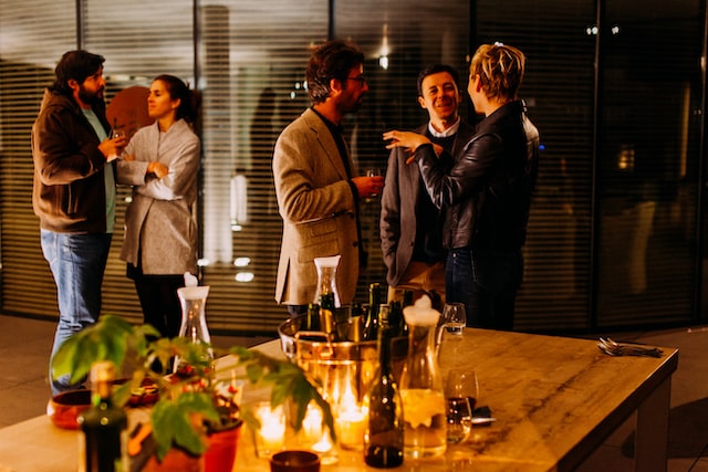 colleagues in casual business attire gather in small standing groups talking and gesticulating at a candlelit office function image at offices.net