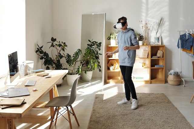 a person in a white painted home office standing on a brown carpet near their desk and wearing a virtual reality headset image at offices.net