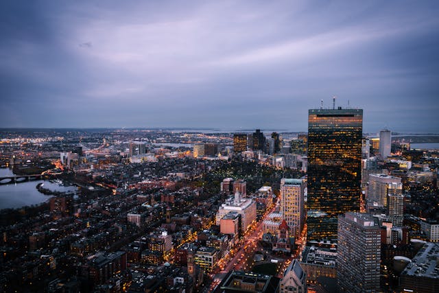 An aerial view across Boston’s cityscape at dusk under a dramatic purple sky with swirling clouds. Image at Offices.net.