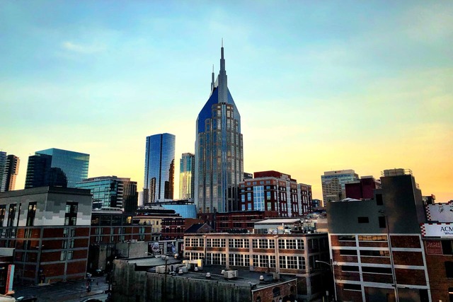 A dusk view from atop a moderately tall building towards the city center of Nashville, Tennessee. The sky is light blue above, fading to yellowy-orange closer to the horizon, while the few taller skyscrapers look shiny as they reflect the last of the sunlight. Image at Offices.net.