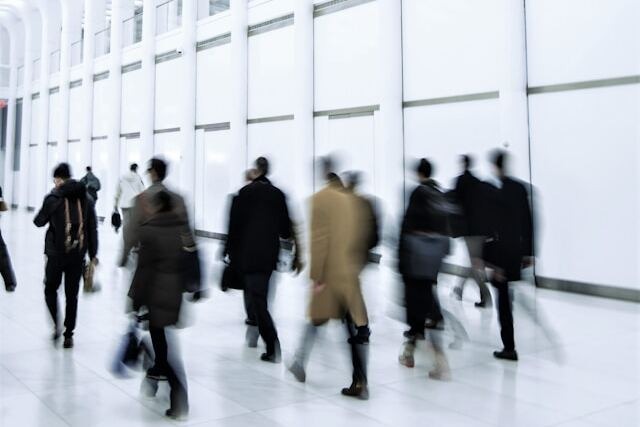 A group of businesspeople walking briskly through a white train station corridor to work. Image at Offices.net.